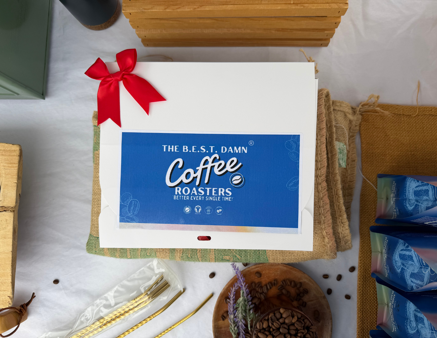 Gift box with a red ribbon and 'The Best Damn Coffee Roasters' logo on a white surface.